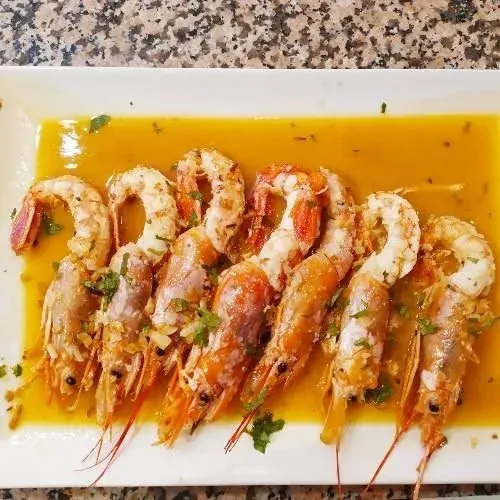 Camarones en salsa, en un plato rectangular blanco. Salsa de naranja con guarnición verde.