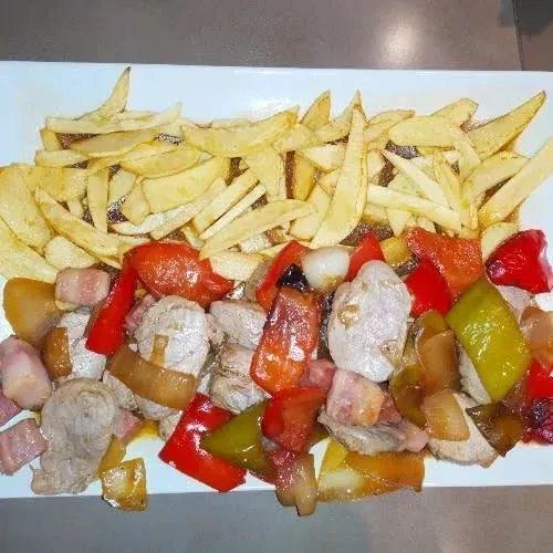 Plato de patatas fritas con cerdo, pimientos rojos y verdes.