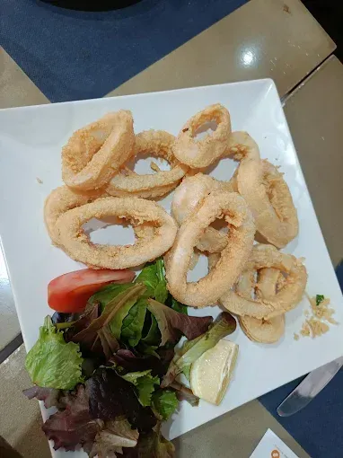Plato de aros de calamar fritos con ensalada y rodaja de limón.