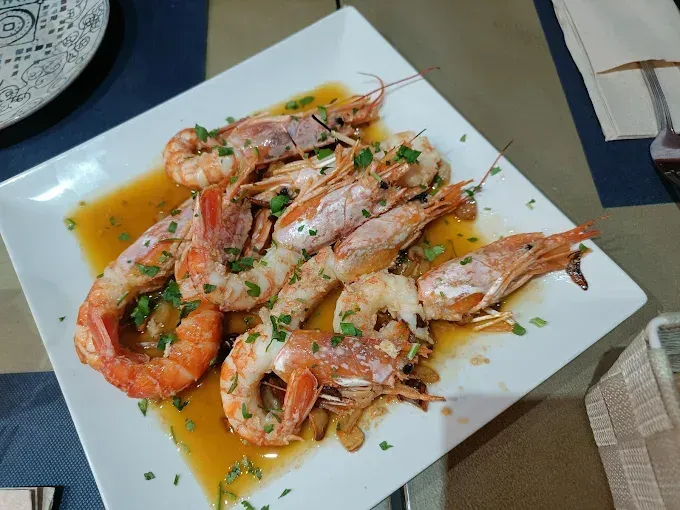 Camarones a la parrilla en salsa, adornados con perejil, servidos en un plato cuadrado blanco.