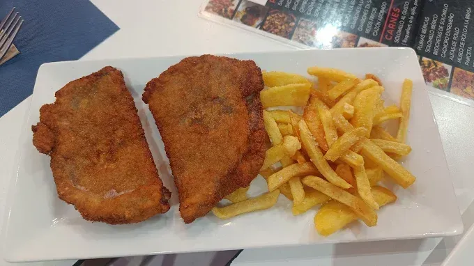 Dos chuletas empanizadas y patatas fritas en un plato rectangular blanco.