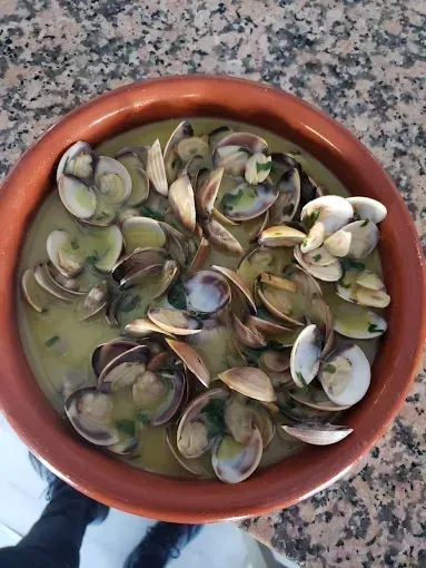 Almejas en caldo, servidas en un recipiente marrón, adornadas con hierbas.