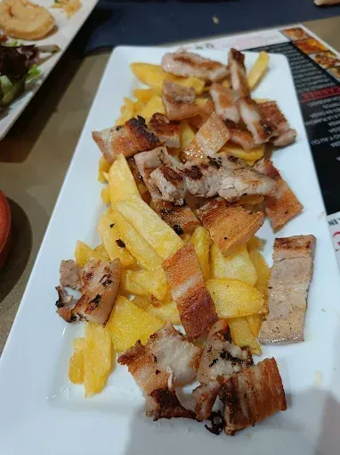 Papas fritas cubiertas con panceta de cerdo a la parrilla en un plato rectangular blanco.