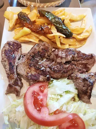 Carne a la parrilla con patatas fritas, pimientos, tomate y lechuga en un plato blanco.