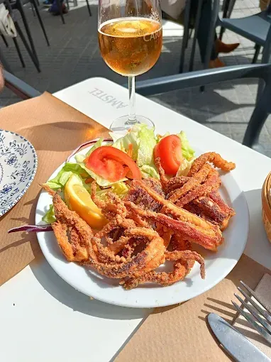 Plato de calamares fritos con ensalada, limón y un vaso de cerveza sobre una mesa.