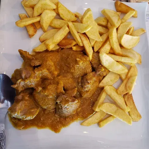Plato de carne en salsa con guarnición de patatas fritas.