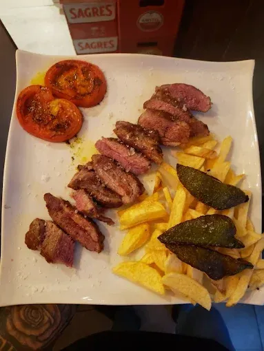 Filete en rodajas con patatas fritas, tomates asados ​​y pimientos en un plato blanco.