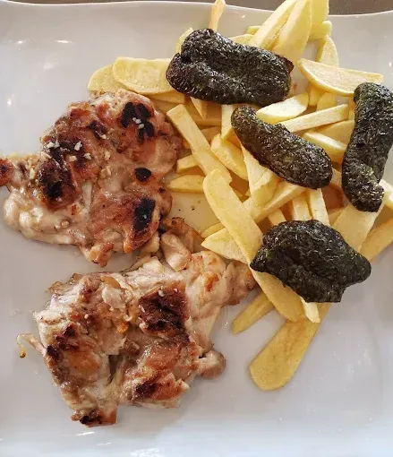Pollo a la parrilla y patatas fritas con objetos negros fritos en un plato blanco.