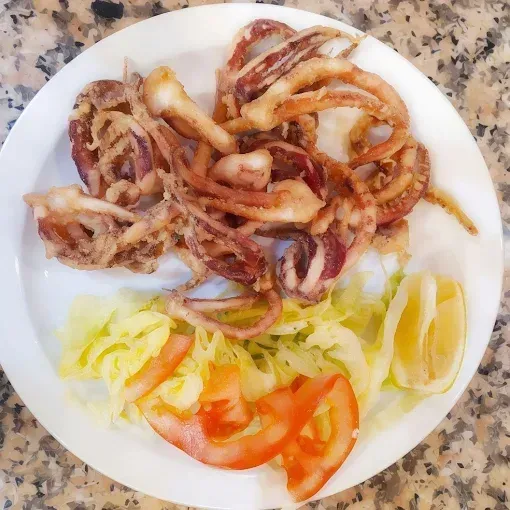 Calamares fritos con limón, tomate y lechuga en un plato blanco.