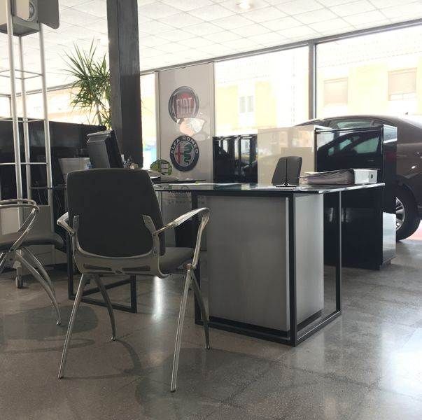 Un coche está aparcado delante de un escritorio y sillas.