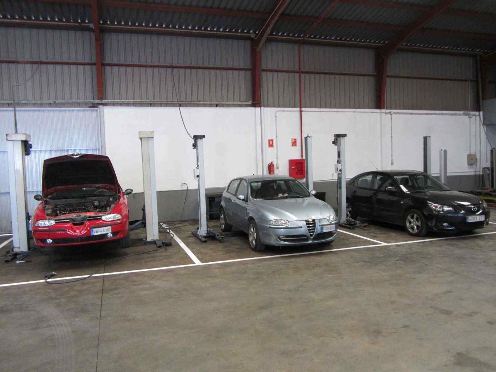 Un coche rojo con el capó levantado está aparcado junto a un coche plateado.