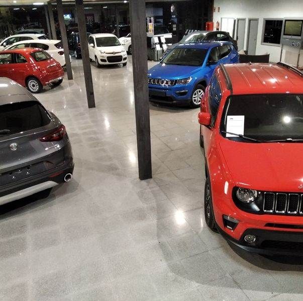 Un jeep rojo está estacionado en una sala de exposición con otros coches.