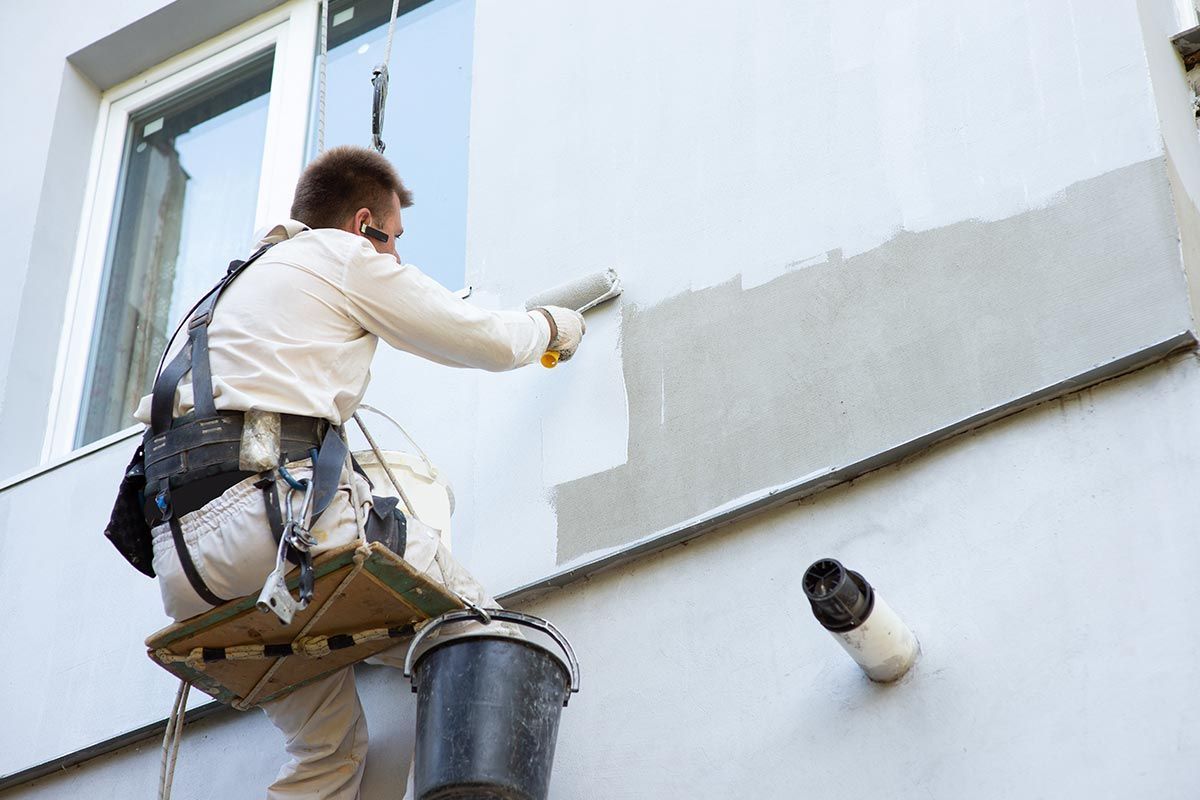 Homme qui peint en hauteur une façade