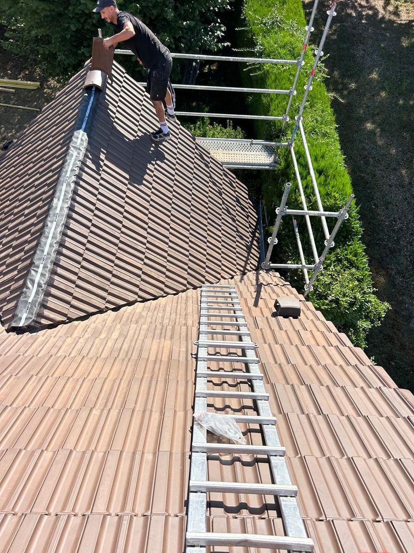 Un couvreur travaille sur un toit de tuiles, présence d'une échelle de toit et d'un échafaudage