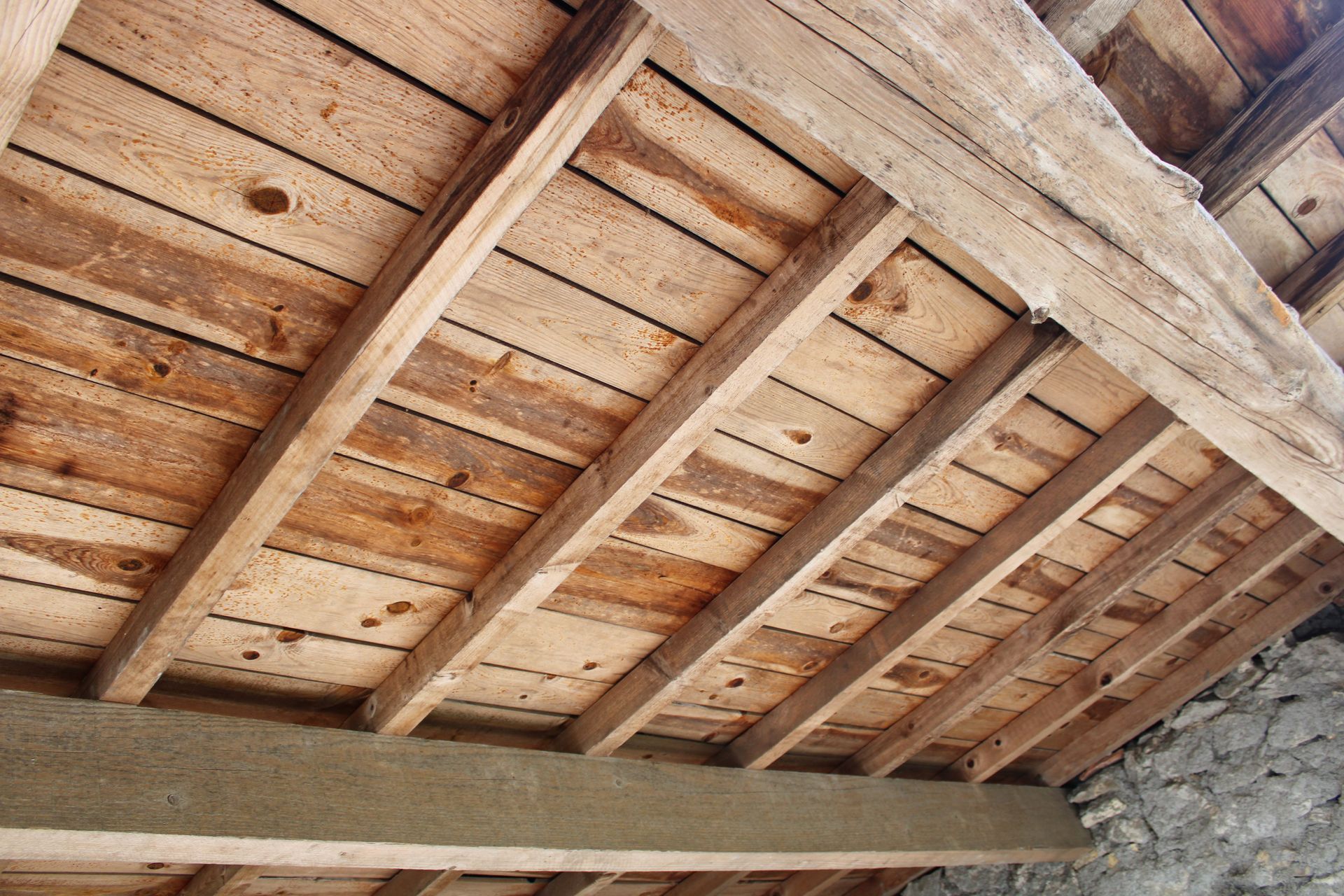 Poutres de plafond en bois avec des planches patinées au-dessus d'un mur en pierre.