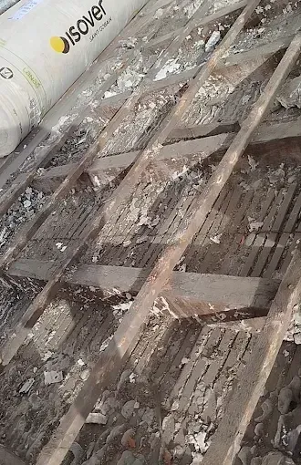 Isolation et charpente en bois recouvertes de poussière et de débris sur un chantier de construction.