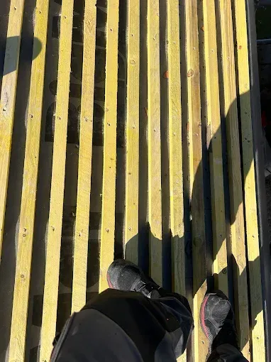 Deux pieds sur une surface jaune à lattes où se projettent de fortes ombres.