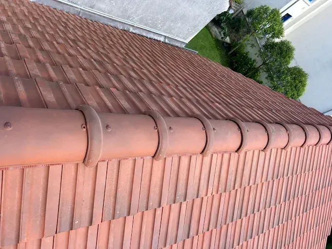 Tuiles de toit en terre cuite avec une faîtière arrondie, vues de dessus, à côté d'un bâtiment blanc.