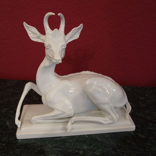 Weiße Keramik-Antilopenskulptur auf einem rechteckigen Sockel vor einer roten Wand.