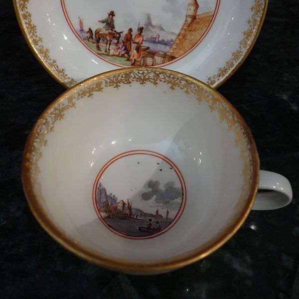 Weiße Teetasse und Untertasse mit Goldrand, mit gemalter Küstenszene.