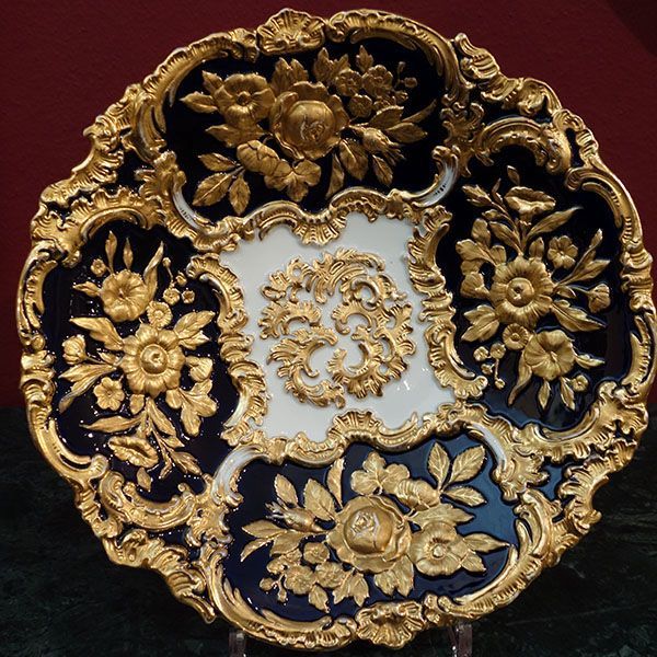 Verzierter Porzellanteller in Gold und Blau mit floralen Reliefdetails.