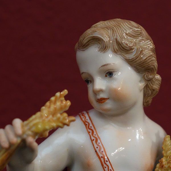 Porzellanengel mit Weizen in der Hand und nachdenklichem Blick vor einem roten Hintergrund.
