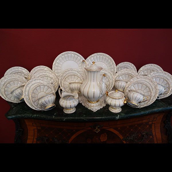 Elegantes weißes Teeservice aus Porzellan mit goldenen Akzenten, präsentiert auf einem Holztisch vor einem roten Hintergrund.