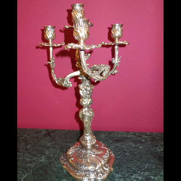 Silberner Kandelaber mit drei Armen und kunstvollem Blumenmuster, der auf einer Oberfläche aus grünem Marmor ruht.