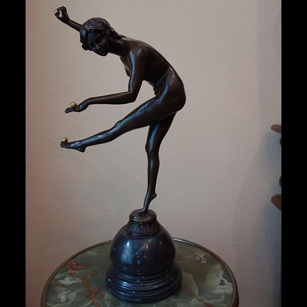 Bronzeskulptur einer Figur, die zwei Kugeln balanciert und jongliert. Sie steht auf einem Sockel auf einem Tisch.