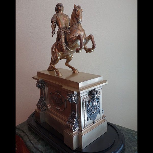 Bronzene Reiterstatue auf verziertem Sockel. Mann auf sich aufbäumendem Pferd; Bronze- und Goldfarben.