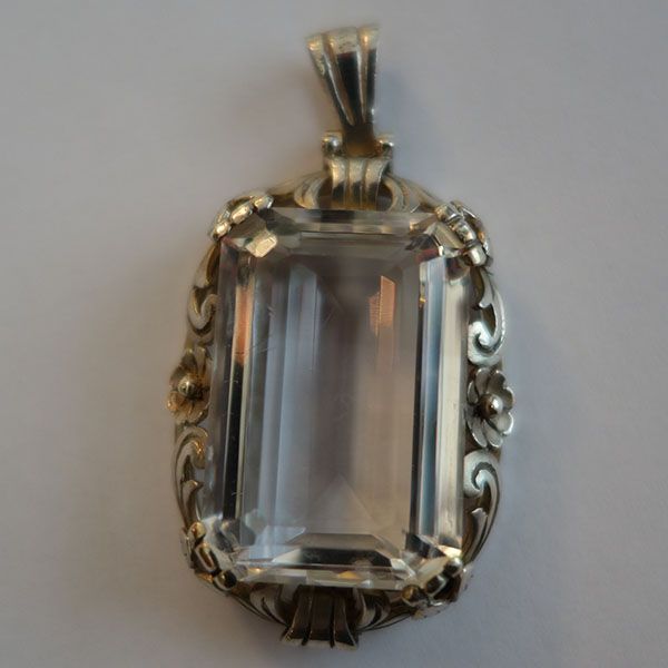 Silberanhänger mit einem rechteckigen, klaren Edelstein, umgeben von floralen Details.