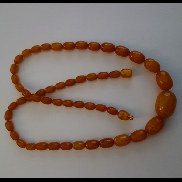 Bernsteinfarbene Perlenkette auf weißem Untergrund, Perlen sind oval geformt.