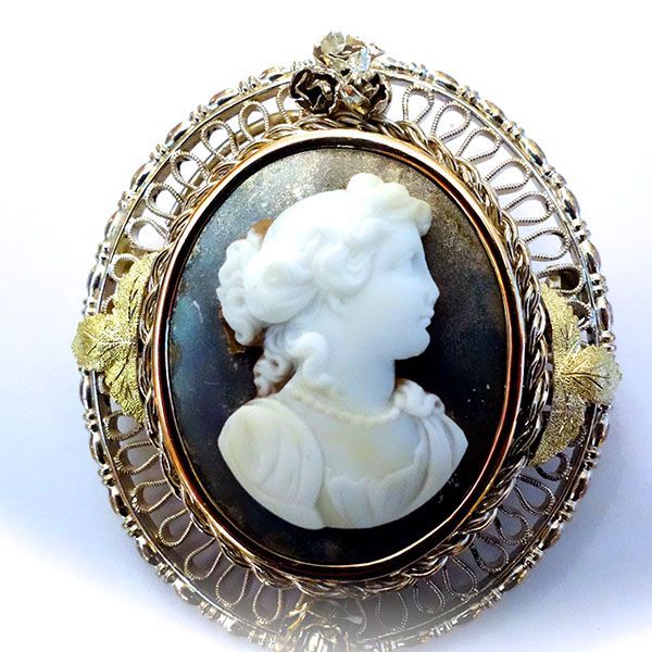 Ovale Kameebrosche mit weißer Büste auf dunklem Hintergrund, umgeben von Goldfiligran und Blättern.