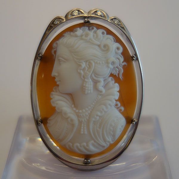 Ovale Kameebrosche mit weißer Profilschnitzerei auf orangefarbenem Hintergrund, eingefasst in einen silbernen Rahmen.