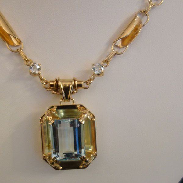 Goldene Halskette mit einem großen, rechteckigen hellblauen Edelsteinanhänger und kleineren klaren Edelsteinen.
