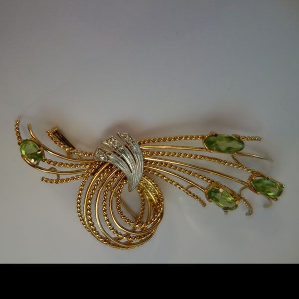 Goldene Brosche mit grünen Edelsteinen und silbernen Akzenten.