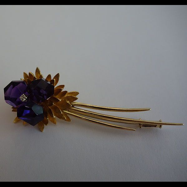 Goldene Brosche mit violetten, facettierten Kristallen in Blumenform.