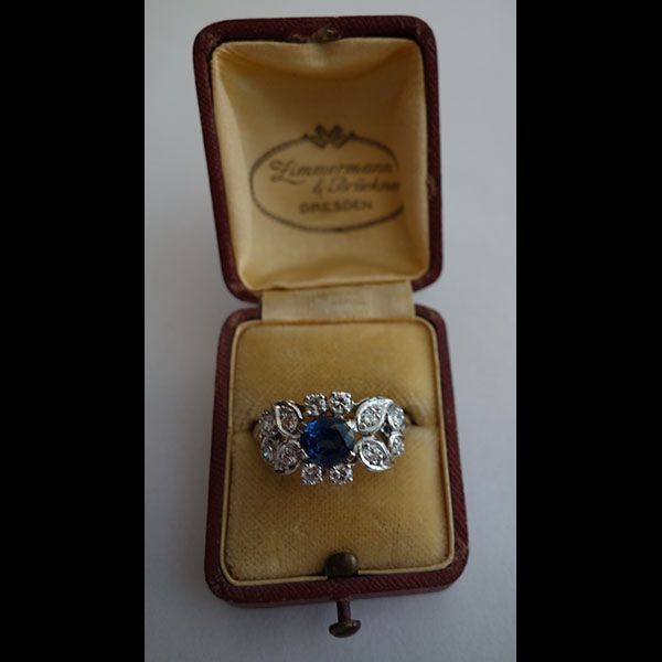 Ring mit blauem Mittelstein und umgebenden weißen Steinen in einer antiken Schmuckschatulle.