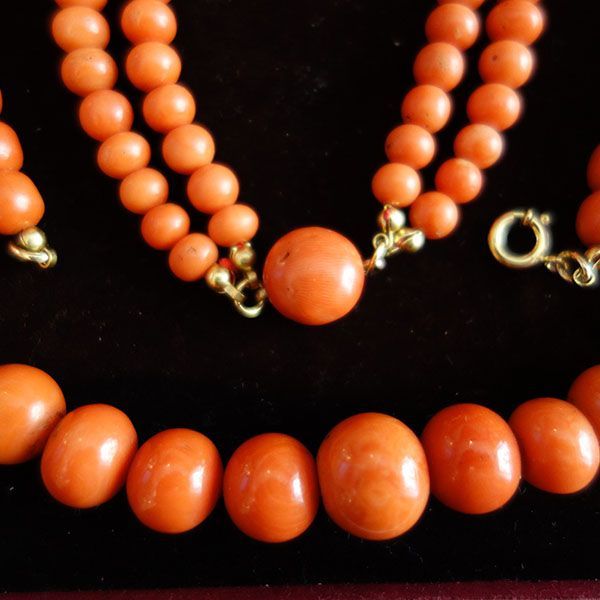 Nahaufnahme eines Sets aus Halskette und Armband aus Korallenperlen mit goldenen Verschlüssen auf dunklem Hintergrund.