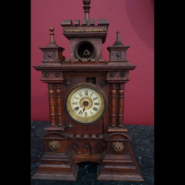 Antike Holzuhr mit rundem Zifferblatt, schlossähnlichem Design und goldenen Akzenten.