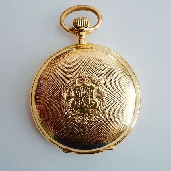 Goldene Taschenuhr mit aufwendig strukturierter Rückseite und verziertem Monogramm.