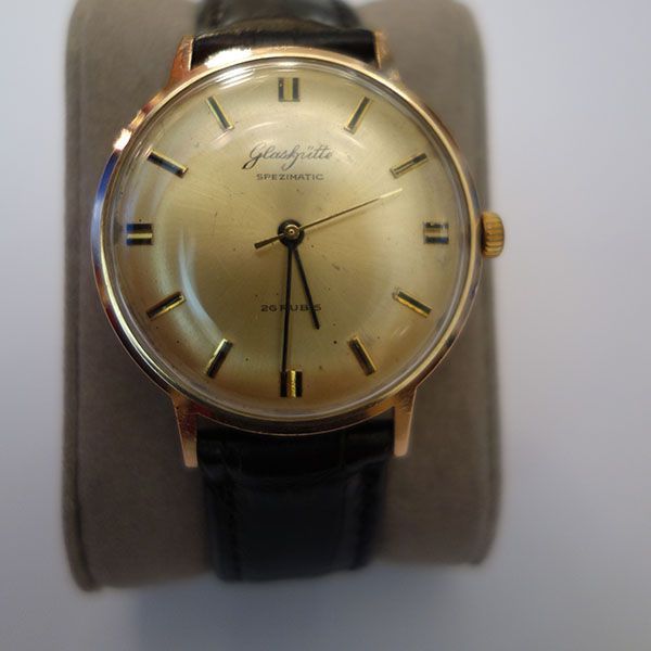 Goldfarbene Glashütte Spezichron-Armbanduhr mit schwarzem Lederarmband auf grauem Untergrund.