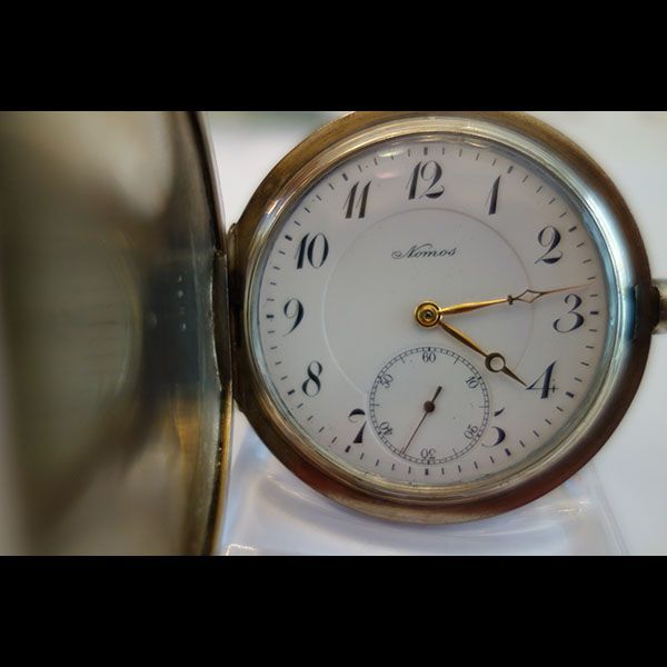 Offene Taschenuhr mit weißem Zifferblatt, goldenen Zeigern und silbernem Gehäuse.