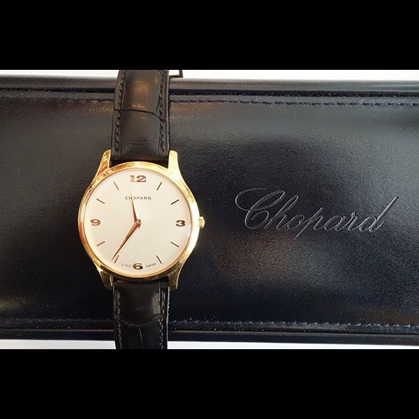 Goldene Chopard-Uhr mit schwarzem Lederarmband auf einem schwarzen Gehäuse mit der Aufschrift „Chopard“.