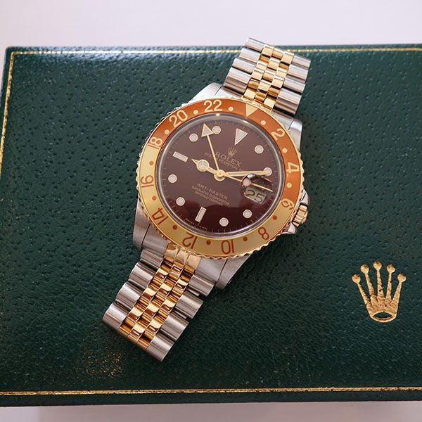 Rolex GMT-Master-Uhr mit goldenem und silbernem Armband und brauner und goldener Lünette auf grüner Box.