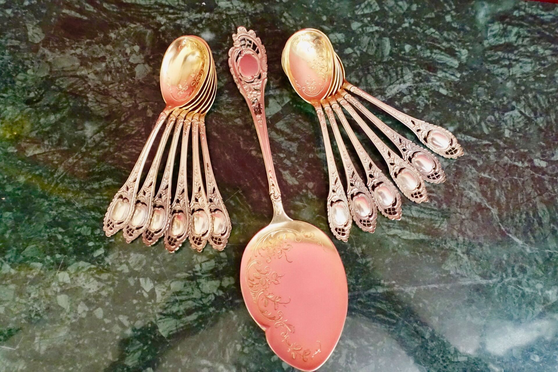 Silberne Servierlöffel mit rosa und silbernen Details, aufgefächert auf einer grün gesprenkelten Oberfläche.