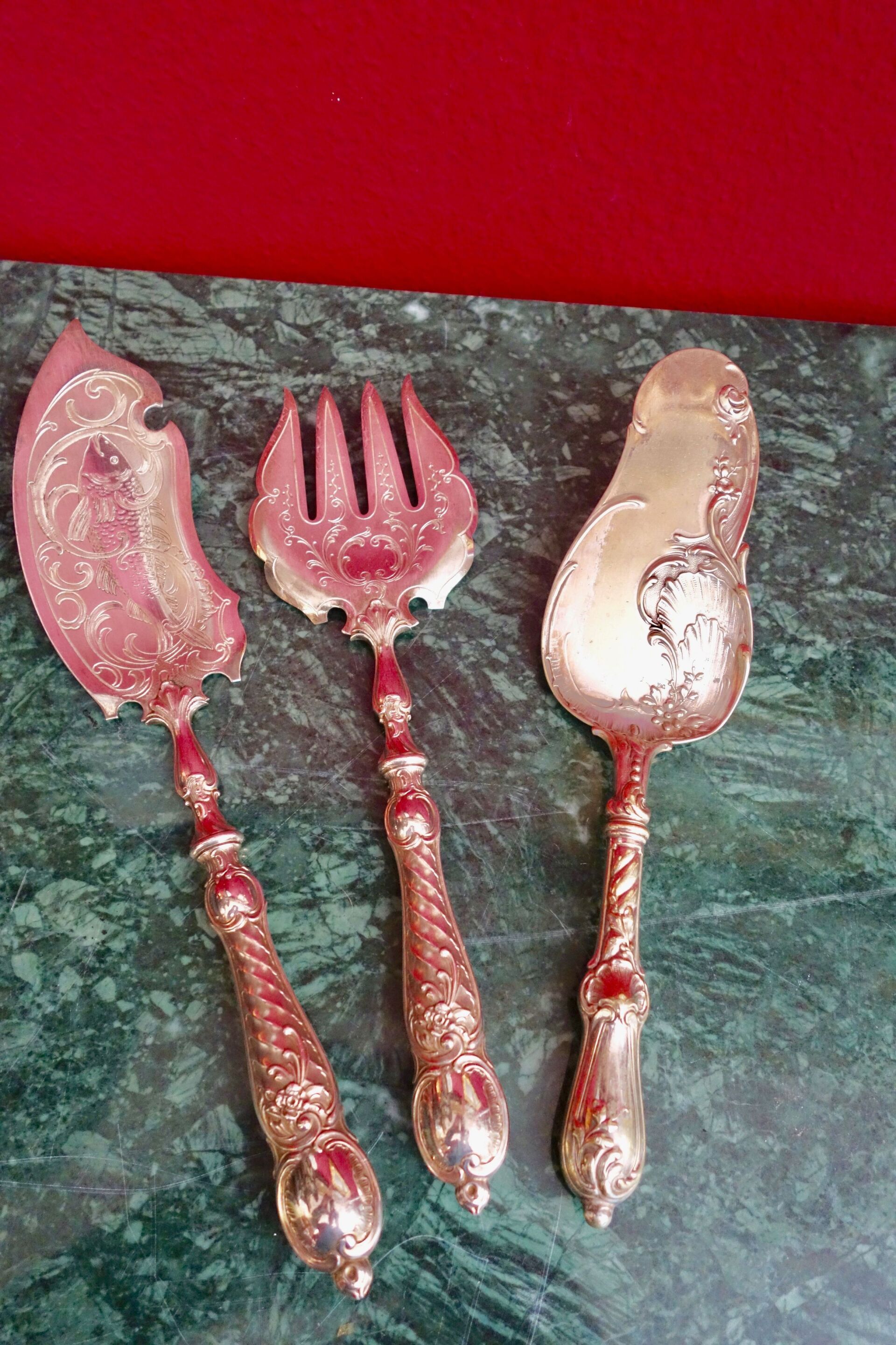 Silbernes Servierbesteck mit verzierten Griffen auf grünem Marmor.