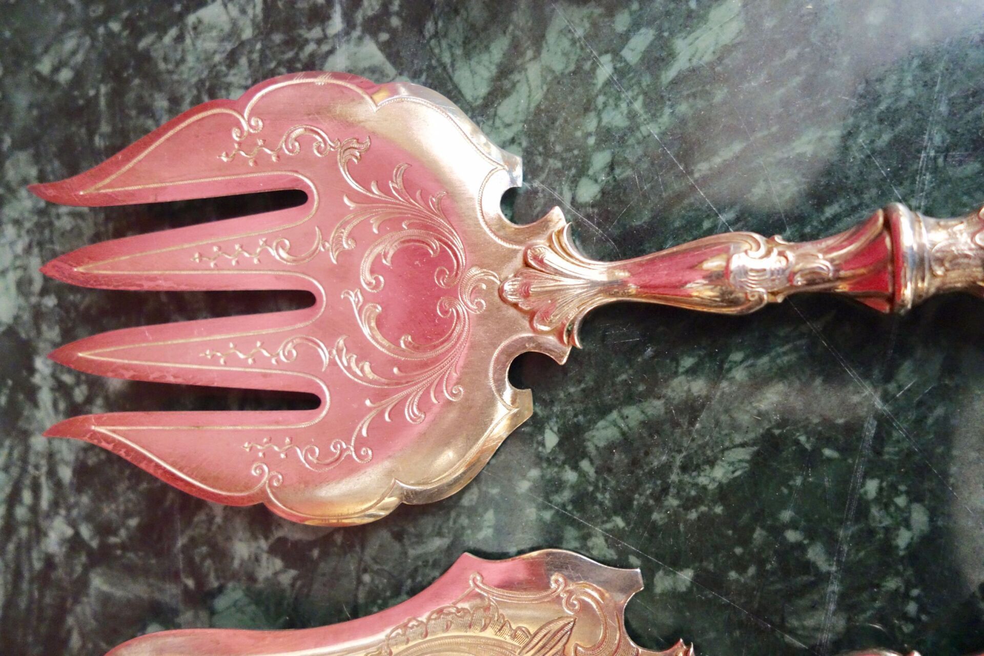 Silberne Serviergabel mit dekorativer Blumenätzung auf rosa Oberfläche.