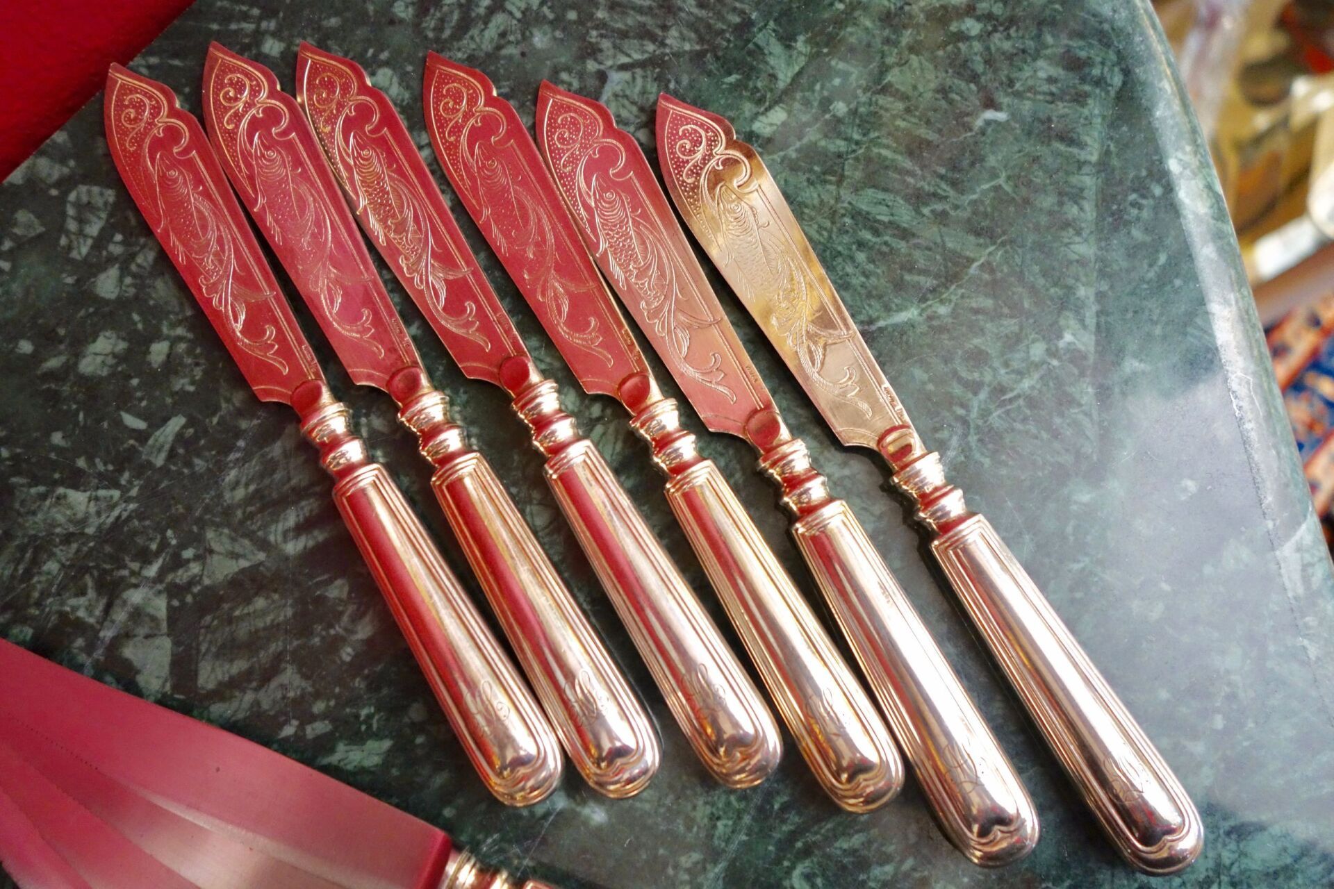 Silberne Buttermesser mit dekorativen Klingen, angeordnet auf einer Marmoroberfläche.