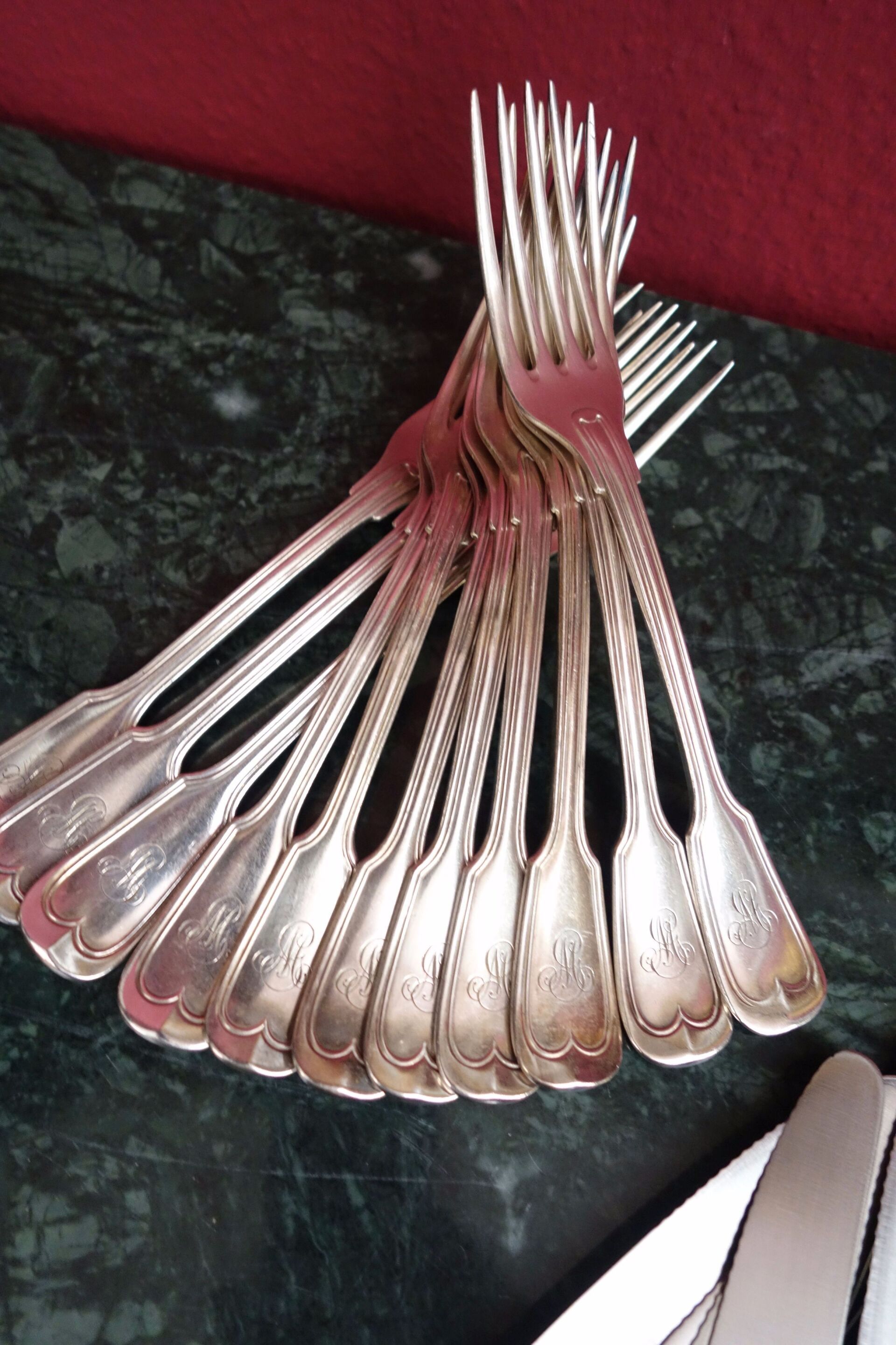 Auf einer dunkelgrünen Fläche angeordnete Silbergabeln, einige mit Initialen auf den Griffen.